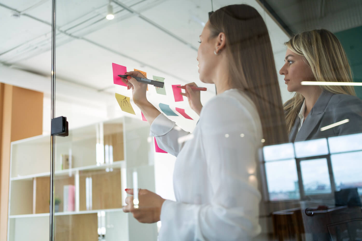 a group of women writing on sticky notes on a glass wall, mapping out the customer journey